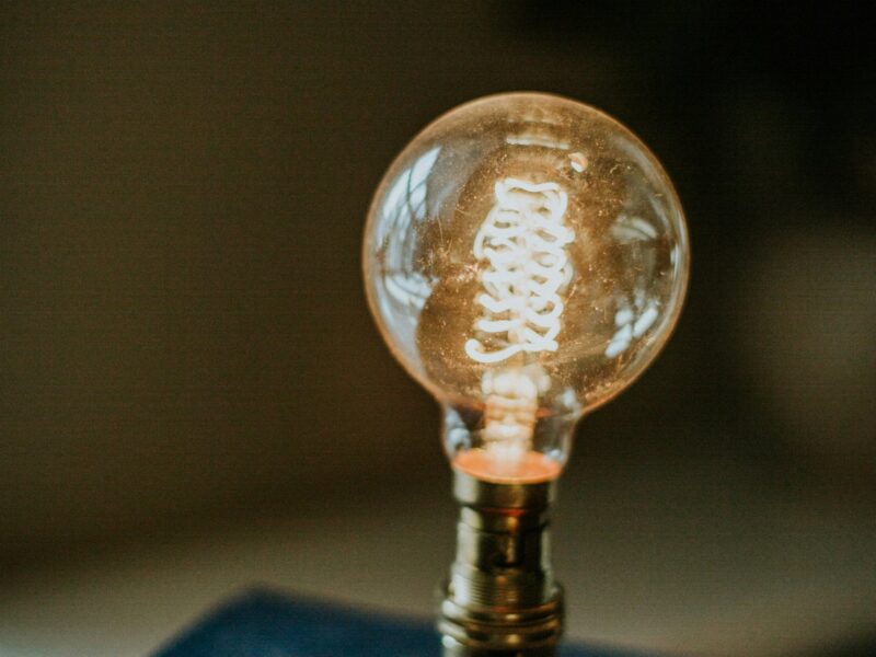 "Eine leuchtende Glühbirne im Edison-Stil steht auf einem Stapel alter Bücher, sinnbildlich für Ideenentwicklung und Wissen."